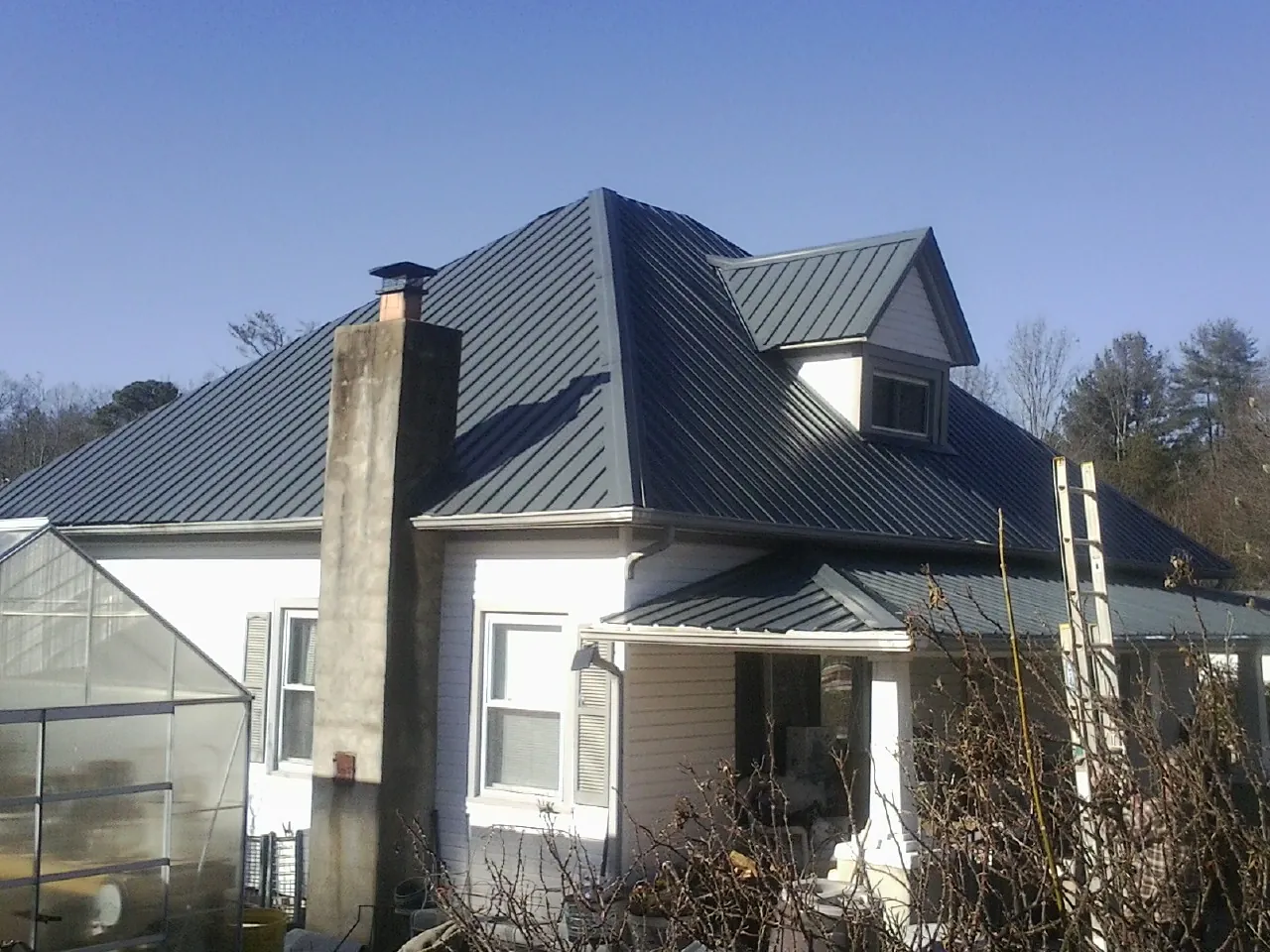 Dark blue standing seam metal roof on a white farmhouse with dormer — Slate & Tile Roof Repair by Roofing Brothers in Jonas Ridge