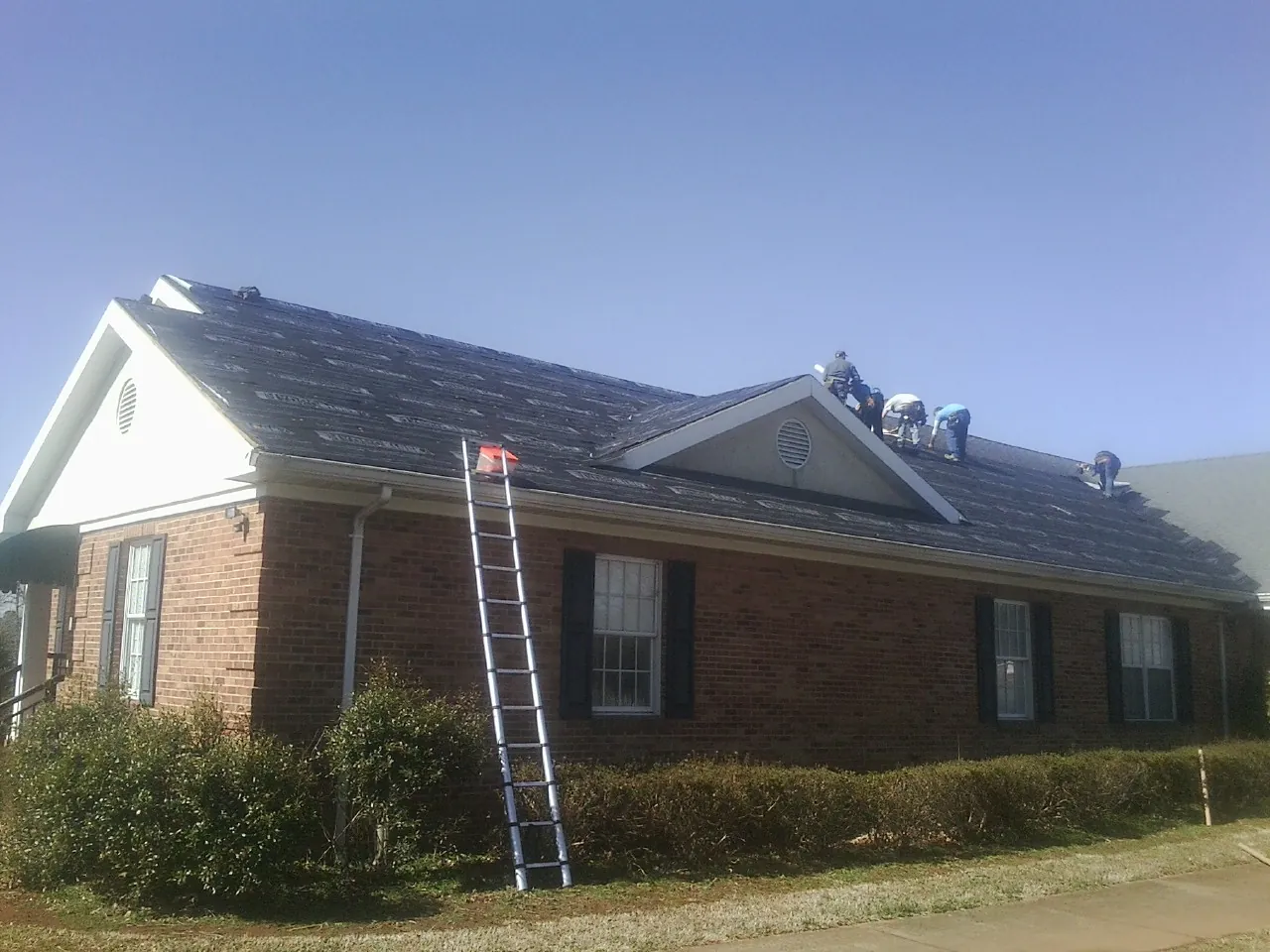 Crew tearing shingles off a brick ranch roof with a ladder set — Metal Roof Repair work by our crew in Jonas Ridge