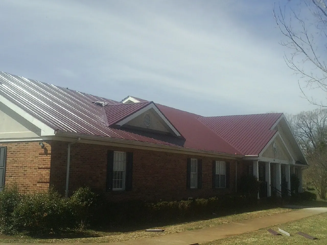 Red metal roof with gabled entries on a long brick building, from a Hail Damage Roof Repair job in Jonas Ridge