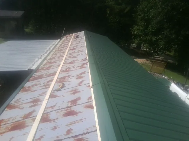 Old rusted panels beside newly installed green metal roofing — Wind Damage Roof Repair by Roofing Brothers in Jonas Ridge