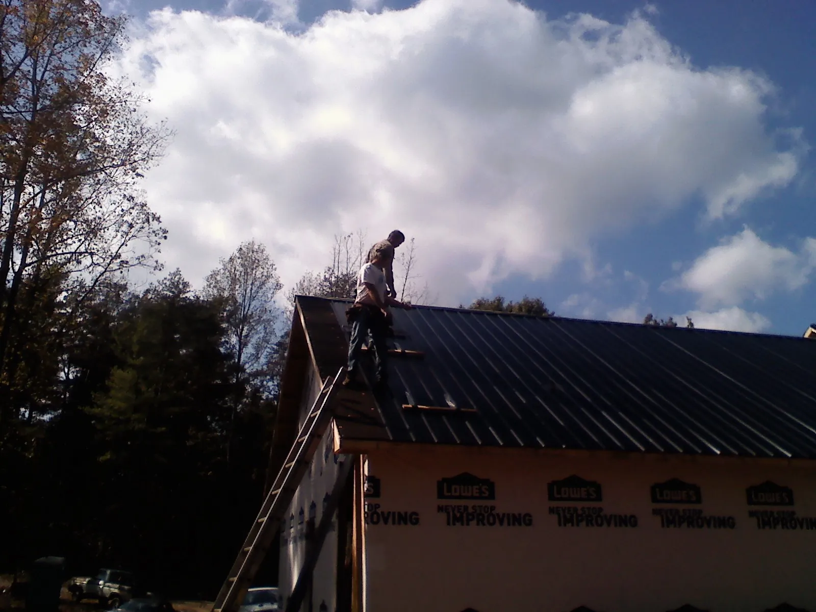 Roofer fastening dark metal panels high against a cloudy sky, from a Roof Inspection job in Jonas Ridge
