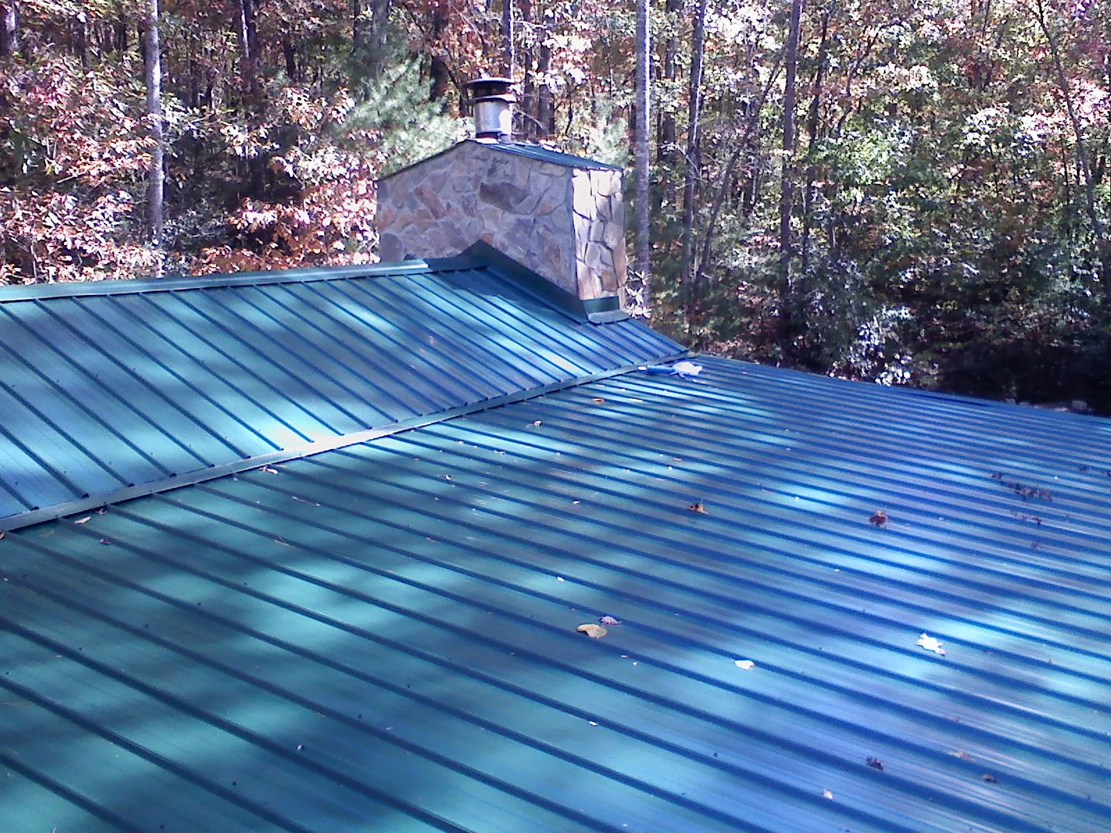 New green metal roof and stone chimney surrounded by autumn woods in Jonas Ridge