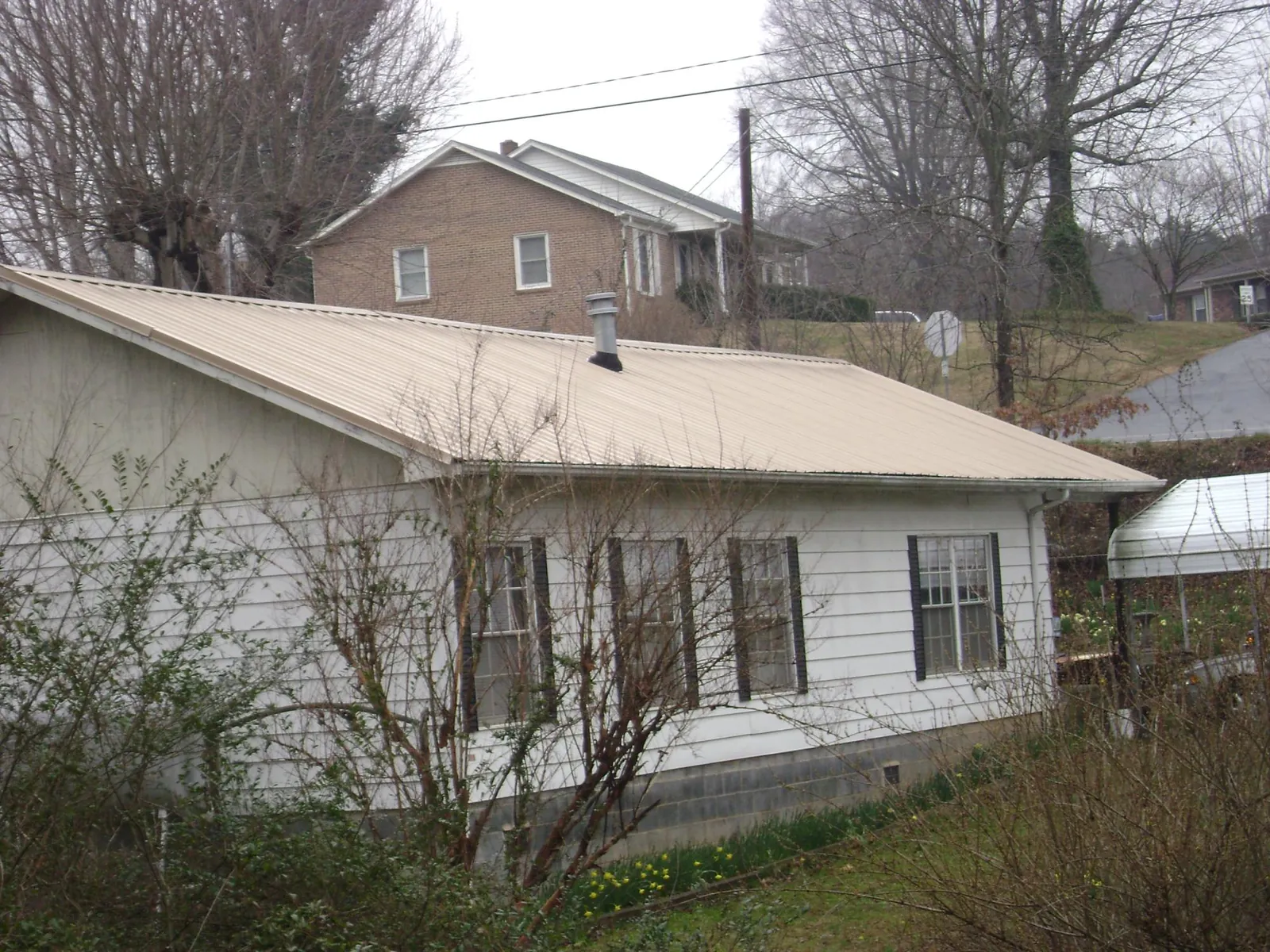 Tan metal roof on a white sided house set into a hillside — Commercial Roofing by Roofing Brothers in Jonas Ridge